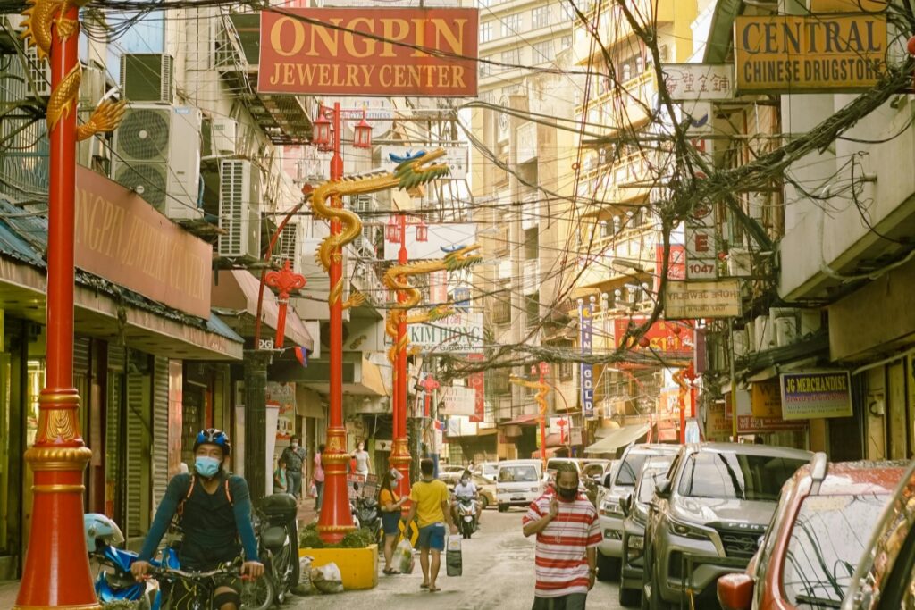 Ang larawan ay nagpapakita ng siksik at masiglang kalye na puno ng mga tinda at advertisement. Nakikita ang "ONGPIN JEWELRY CENTER" at iba pang mga palatandaan ng negosyo, kasama na ang "CENTRAL CHINESE DRUGSTORE". May mga tao rin na naglalakad, nagbibisikleta, at nagmamaneho ng sasakyan. Tulad ng kalye na puno ng iba't ibang uri ng negosyo, ang pinakamabisang social media platforms para sa e-commerce ay nag-aalok ng iba't ibang pagkakataon para sa mga negosyante. Ito ay nagiging daan upang maabot ang malawak na merkado at maipakilala ang kanilang produkto at serbisyo.
